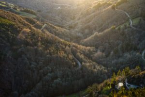 Aerial view of a forested valley with winding roads and power lines across rolling hills at sunset.